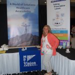 Amanda Tolson standing in front of En-Vision America and ScripTalk Banners at the exhibit table