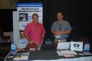 Dr. Brett Mills standing behind the EyeHelpLowVision exhibit table